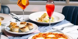 pizza on a table with a cocktail and some rolls on another plate