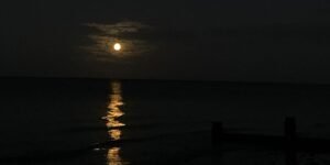 autumnal equinox rituals - the moon in a black sky reflected on water
