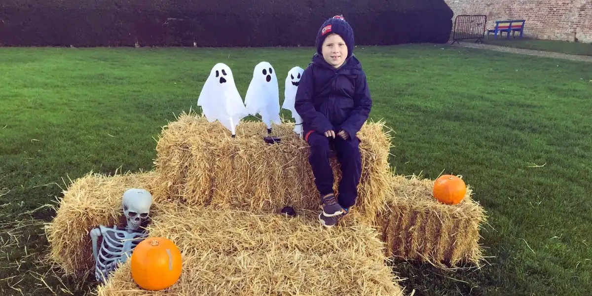 boy sitting on hay bales with small ghost figures and pumpkins