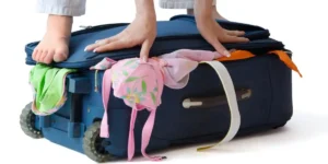 overstuffed suitcase with a woman standing on it to get it closed