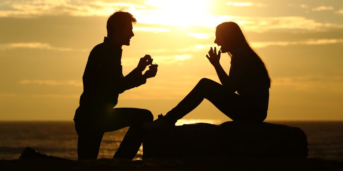 perfect engagement trip couple silhouetted at sunset, man on one knee proposing