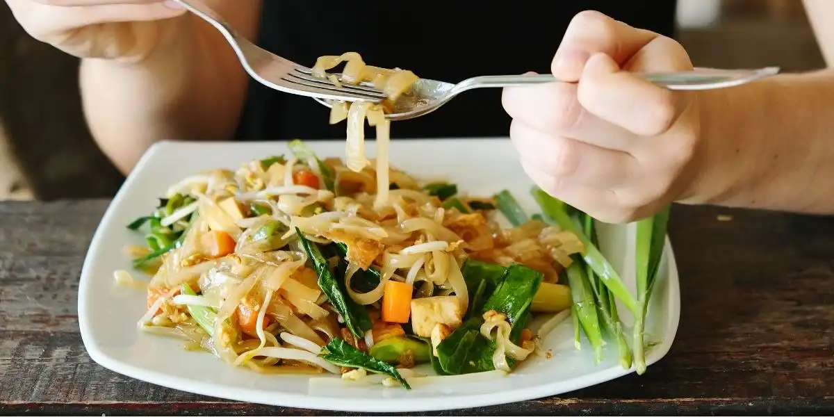 A person eating a portion of Pad Thai at a restaurant at the Ao Sane beach at Phuket, Thailand