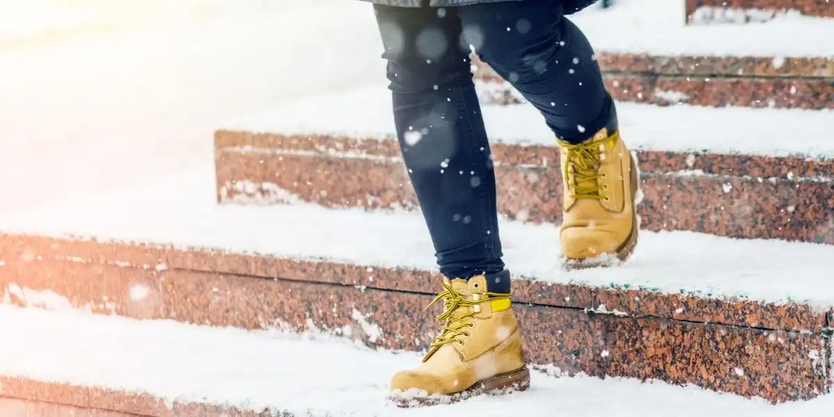 travel essentials for winter - A young woman in yellow leather boots descends on snowy granite steps in an urban environment.