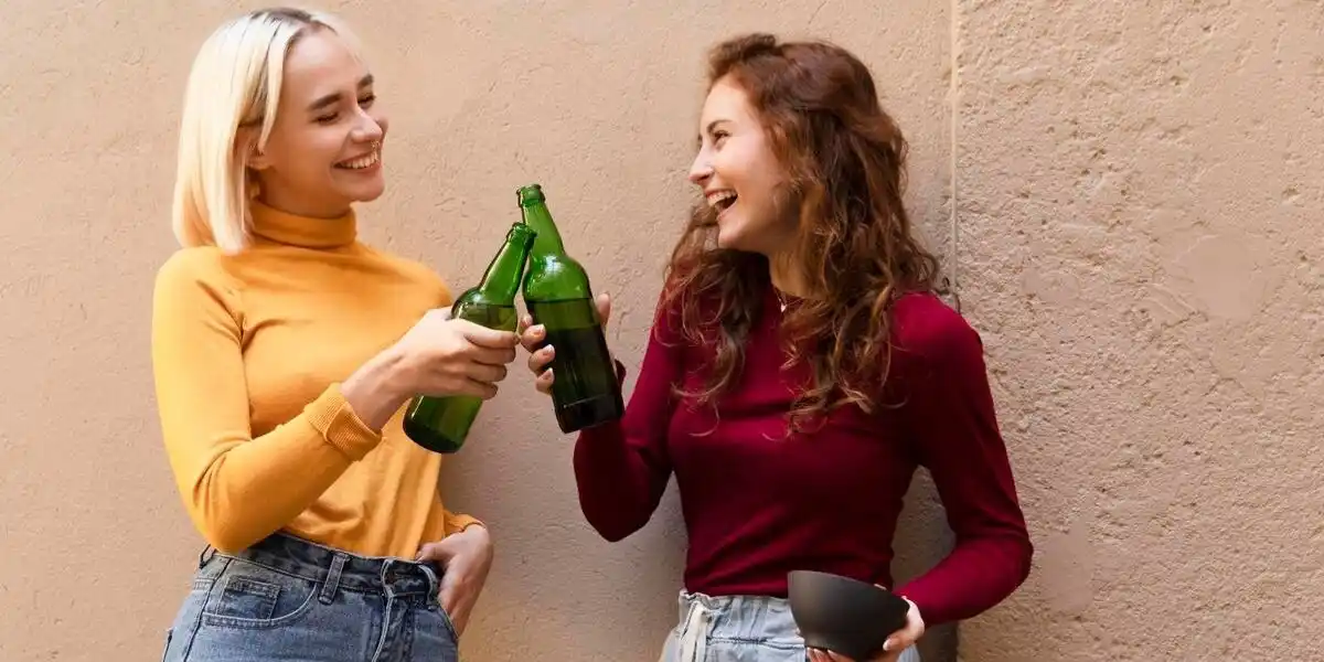 two young women enjoying a CBD drink in an outdoor setting in front of a wall