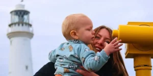 woman and small child looking at a telescope in front of lighthouse
