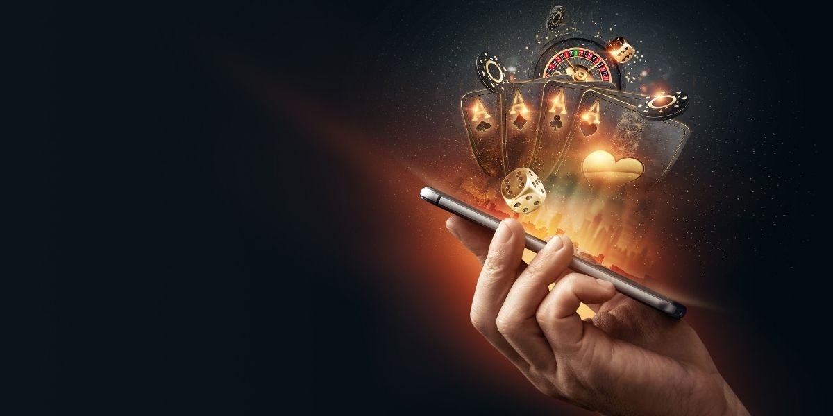 Creative background, online casino, in a man`s hand a smartphone with playing cards, roulette and chips, black-gold background. Internet gambling concept
