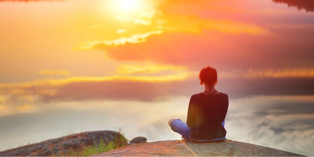 a woman meditating on mountain top at sunset