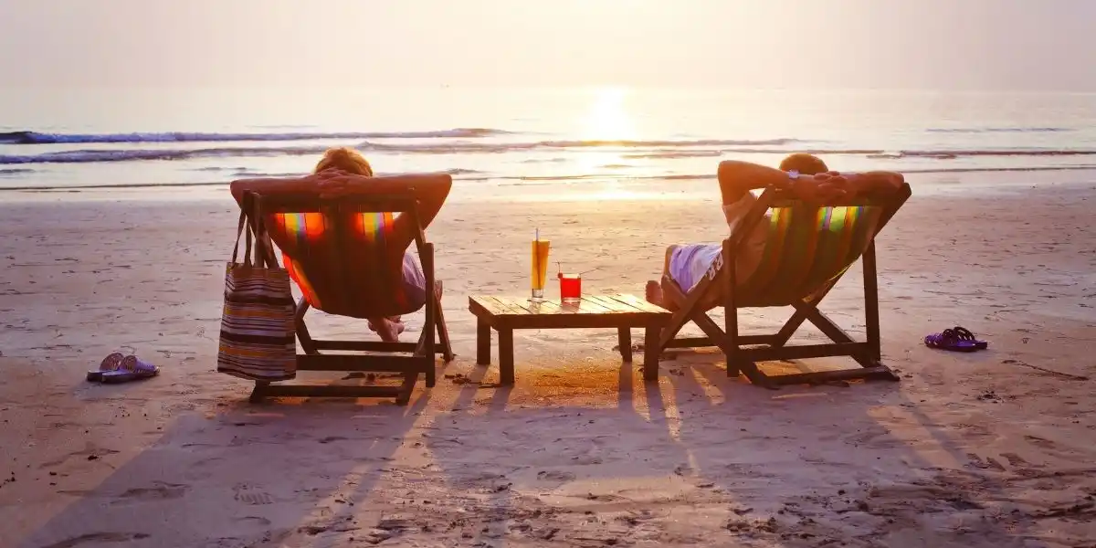 two people on a beach at sunset with a cocktail each