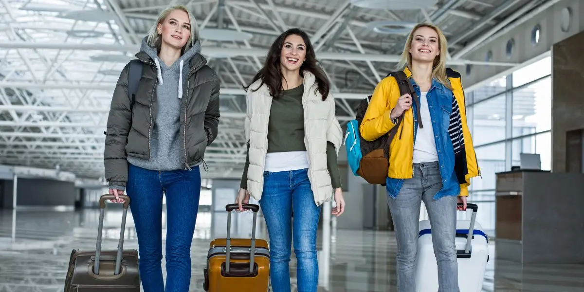 Portrait of three women with baggage moving in the direction of airliner. Their faces expressing amusement