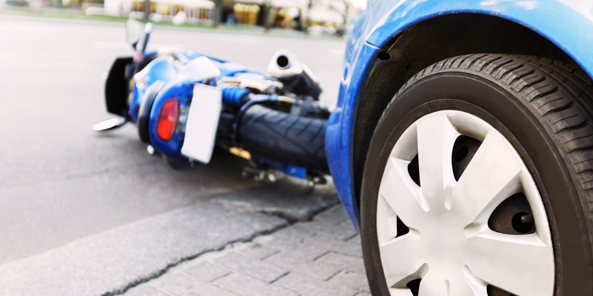 a blue car with a motorcycle lying on the floor in front of it