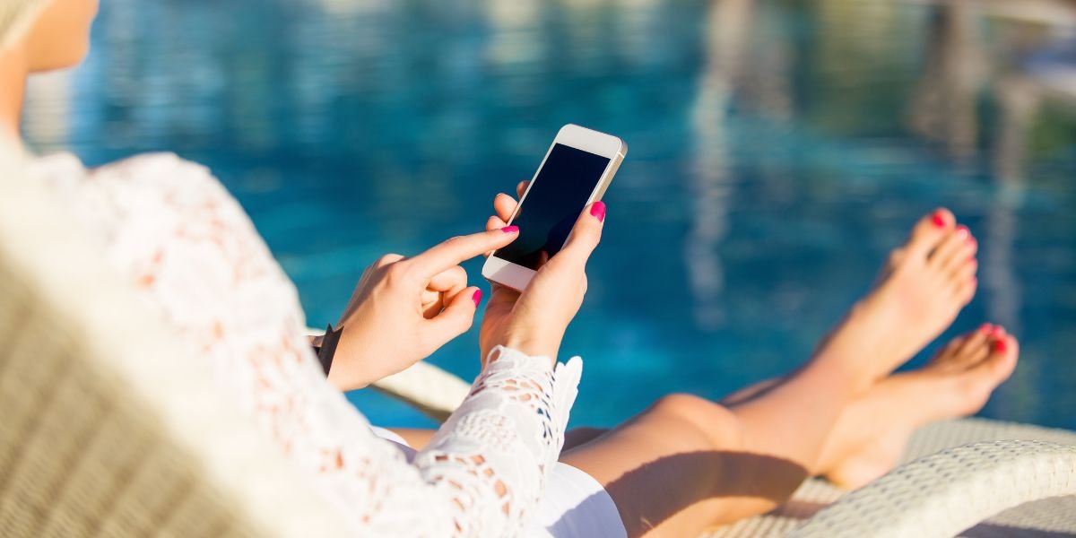 Woman sitting in deck chair and using mobile phone, travel planning concept