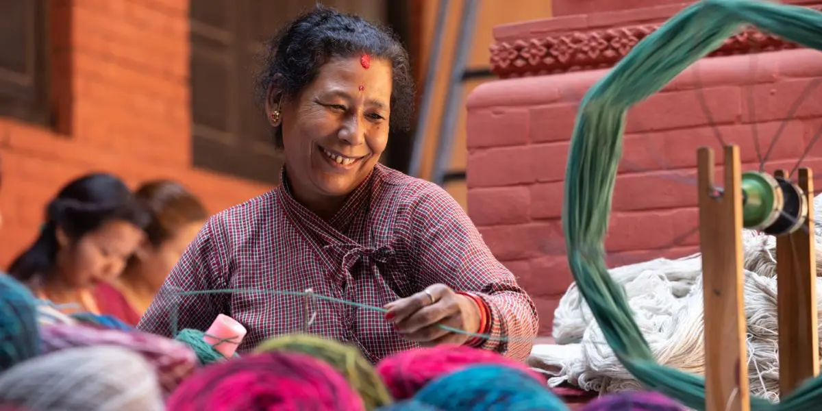 A lady in a colourful room smiling while she knits