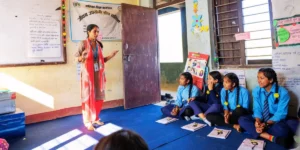 a teacher in a classroom in Nepal with pupils sitting on the floor enjoying the lesson