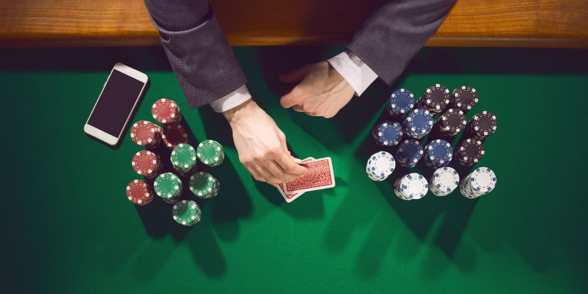 Elegant male poker player with smartphone looking at his cards with piles of chips all around