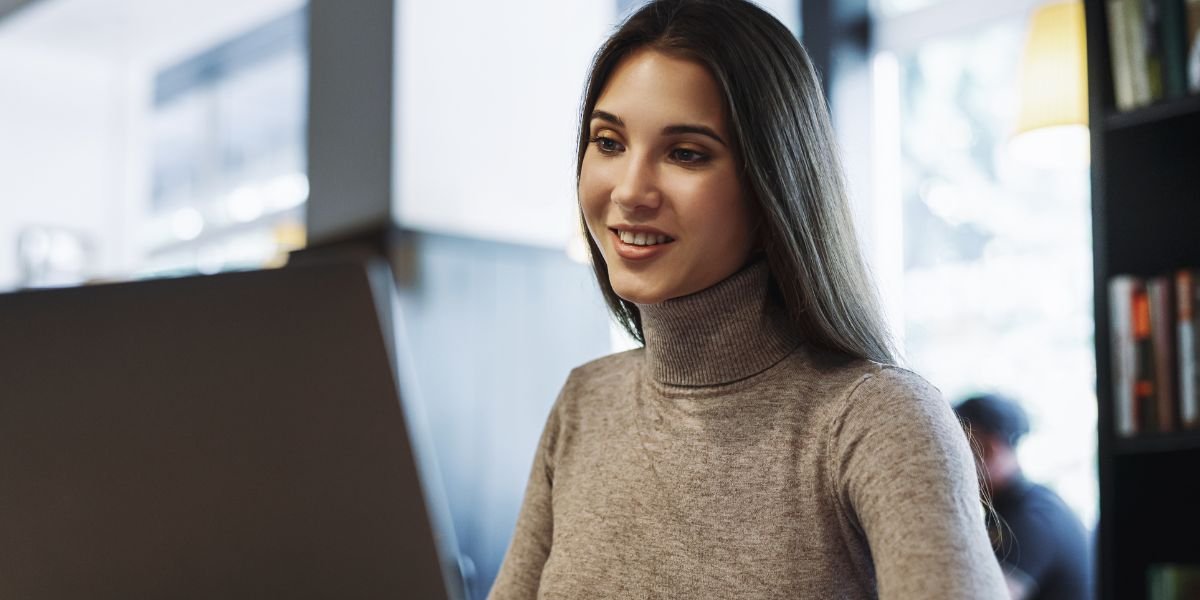 business woman sits at table in front of laptop, works remotely while in cafe. Freelancer software tester discussing work using video communication