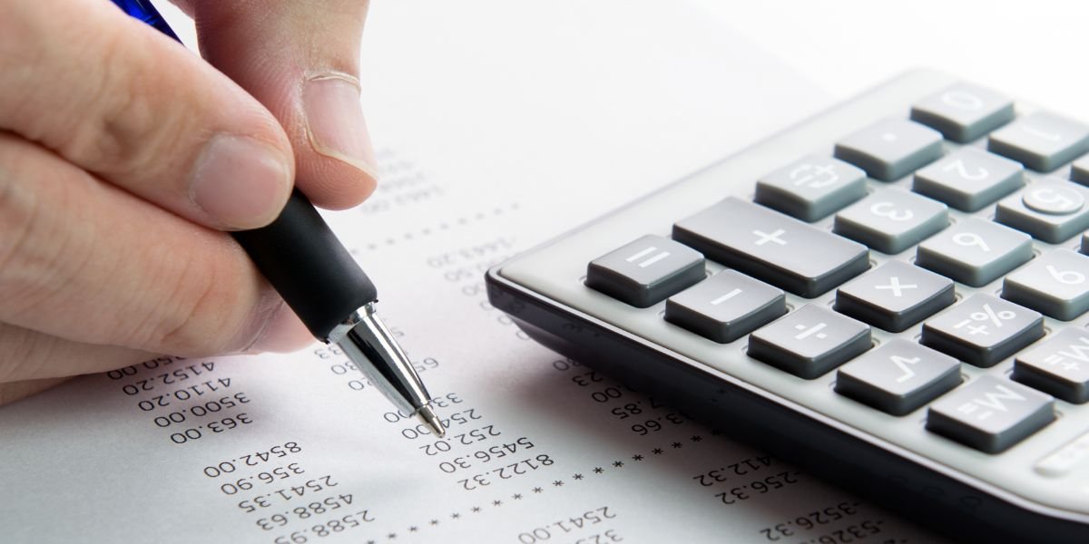 finances concept. a list of numbers with a calculator and someones hand holding a pen