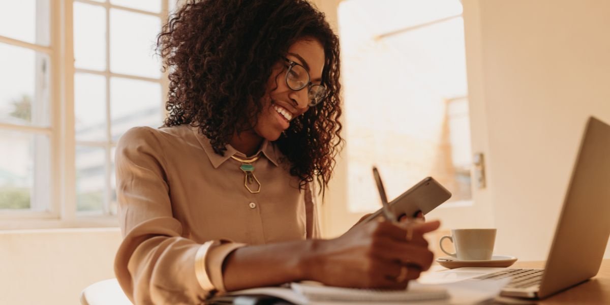 Businesswoman sitting at home on a table looking at tablet pc and making notes while working on laptop. time money freedom