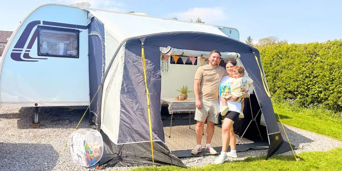 young family standing outside a caravan awning in the sunshine