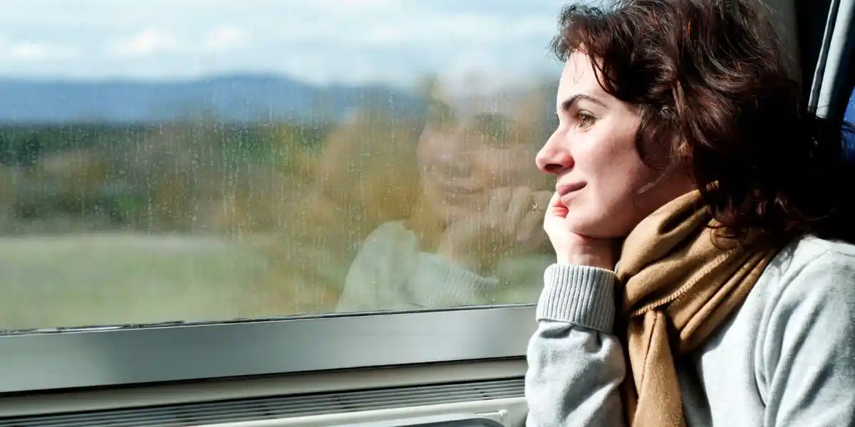 woman travelling by train and looking out of window - solo and slow travel concept