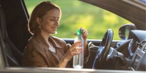 Woman driver drinks water from a refillable bottle in her car, driving on holiday in the uk