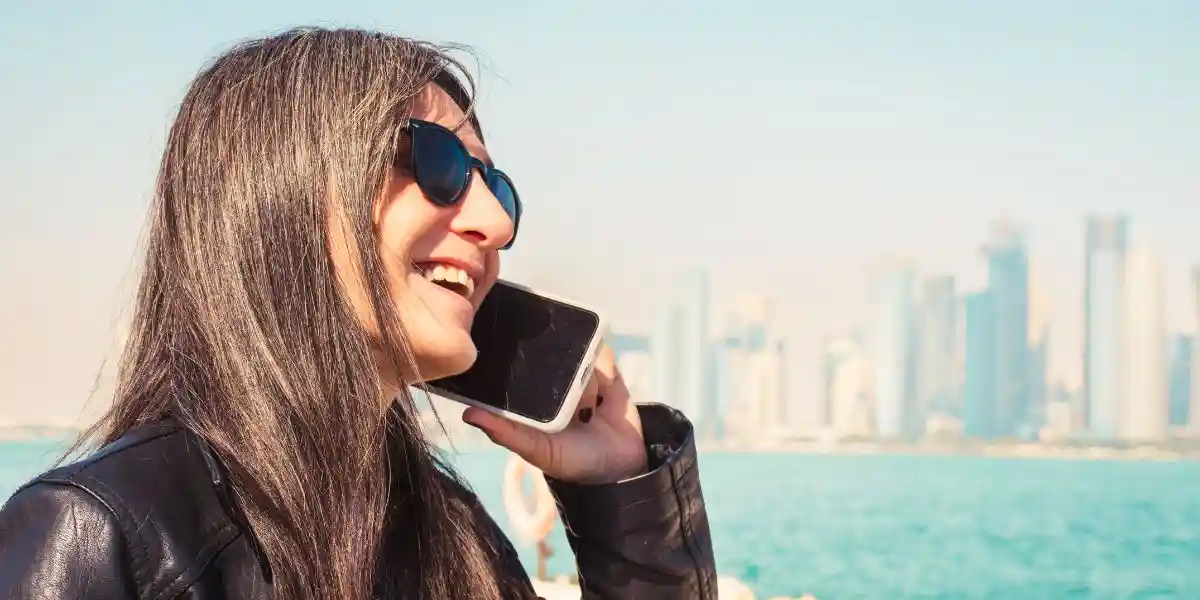 woman chatting using smartphone esim travel with West Bay skyline background Corniche waterfront. Roaming internet communication