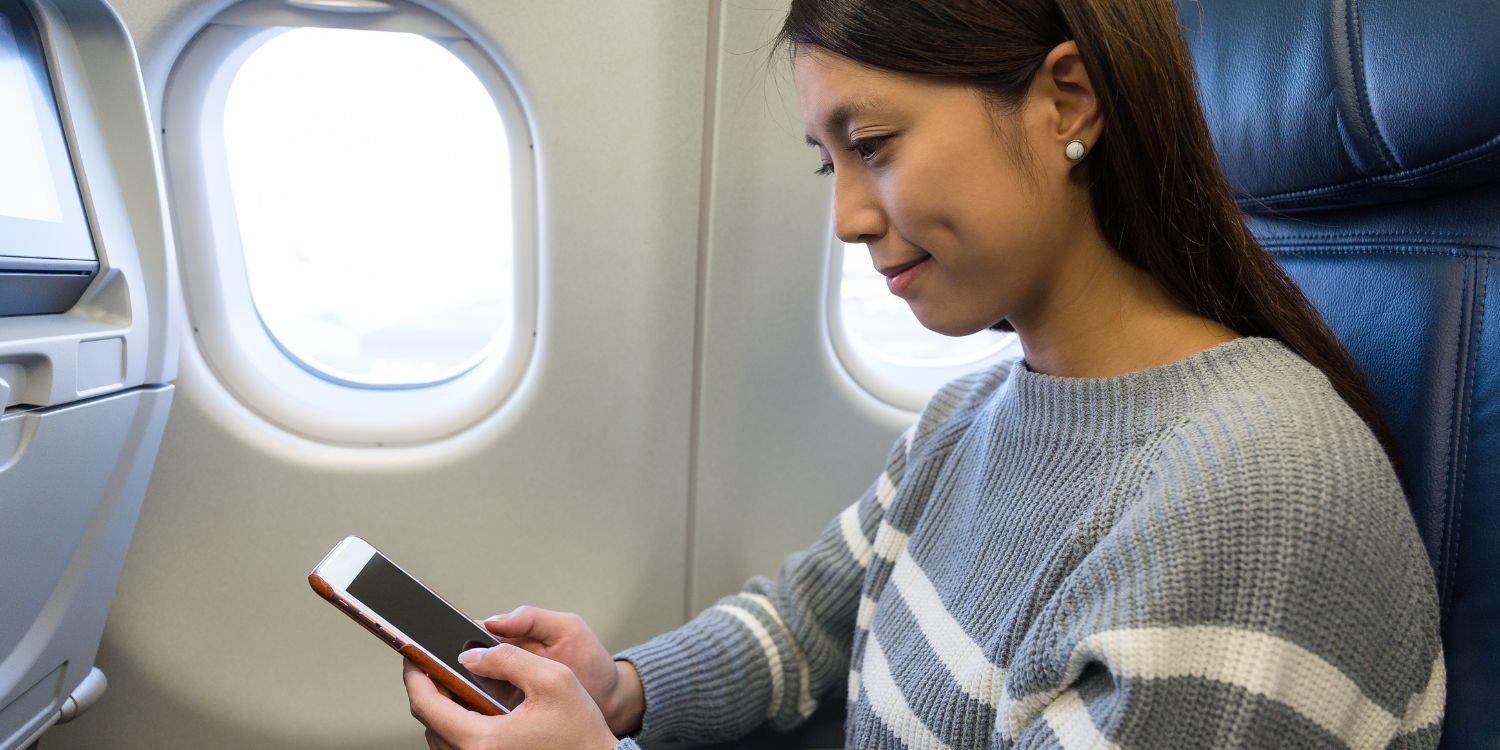Woman using mobile phone in the plane cabin, getting her esim ready for her holiday