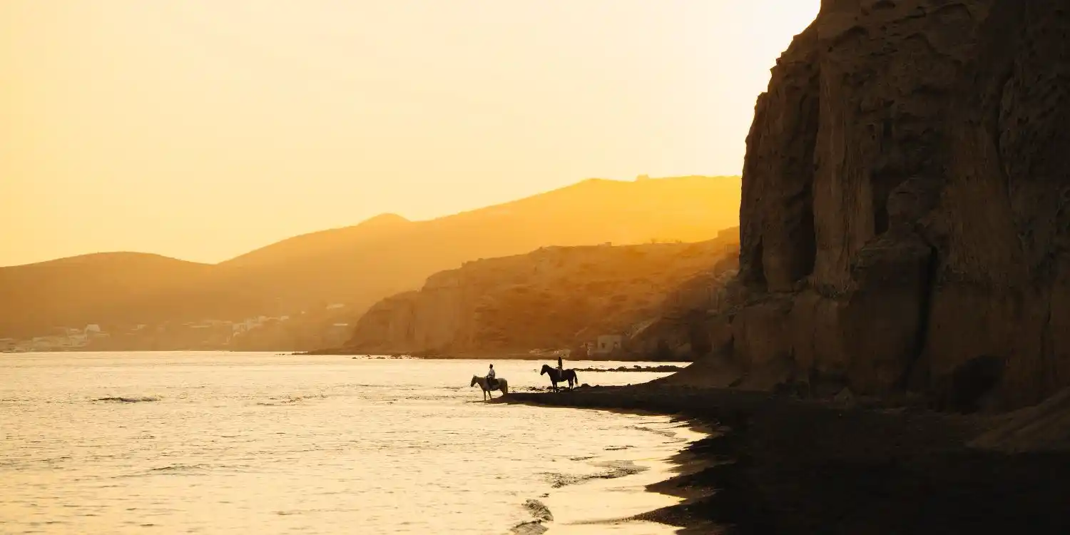 a santorini sunset over the sea with horses silhouetted