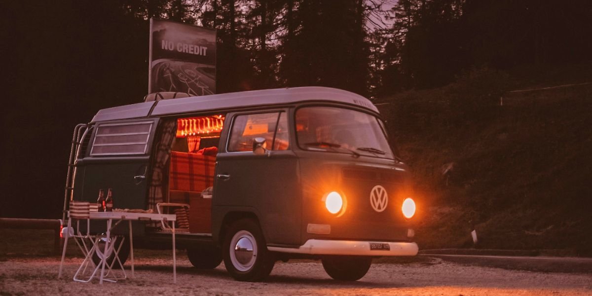an autumn scene with a campervan and it's headlights on