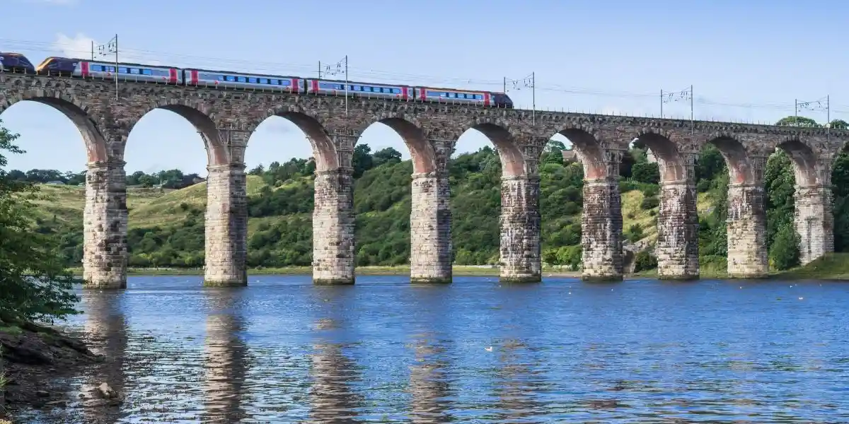 a train going over a long bridge across the river tweed