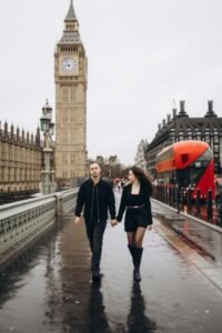 Couple walking hand in hand across a wet Westminster Bridge with Big Ben and a red London bus behind