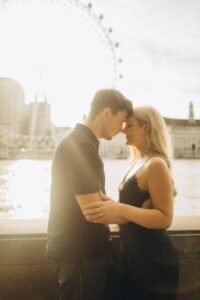Couple touching foreheads on the Victoria Embankment in golden light, London Eye across the Thames